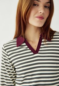 Langetermijnsromper gemaakt van een zachte stof, met zwart-wit gestreept ontwerp en een kastanjebruine kraag en V-hals.