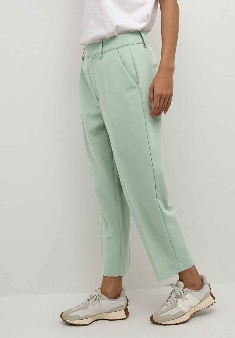 Pantalon ajusté vert menthe avec plis à l'avant, poches latérales et longueur cropped, associé à des baskets gris clair avec une semelle texturée.