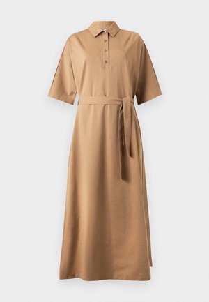 Femme portant une robe midi couleur camel avec un col, une patte de boutonnage, des manches larges, une ceinture à la taille et des sandales noires à talons hauts.