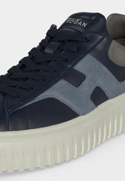 Baskets Hogan bleu marine et gris avec semelle blanche texturée, panneaux en cuir et daim, et lacets, inclinées pour montrer les détails latéraux et supérieurs.