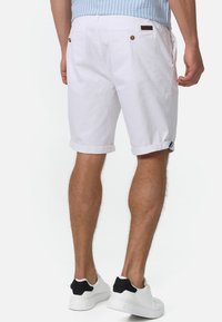 Shorts bianchi in cotone con risvolti, dotati di chiusura a bottone e due tasche posteriori. Abbinati a sneakers bianche con accenti neri.