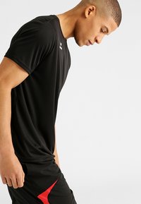 T-shirt de sport noir en tissu léger, avec un col rond et des manches courtes. Équipé d'un petit logo sur l'épaule.