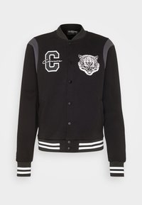 Svart varsity-jacka med vit broderad tiger och detaljer med bokstaven "C", tryckknappar, randiga ribbade muddar och krage. Mjuk tyg.