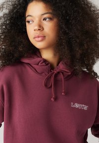 Mörkröd hoodie i mjukt tyg, med dragsko i huvan och en liten broderad Levi's-logotyp på bröstet.