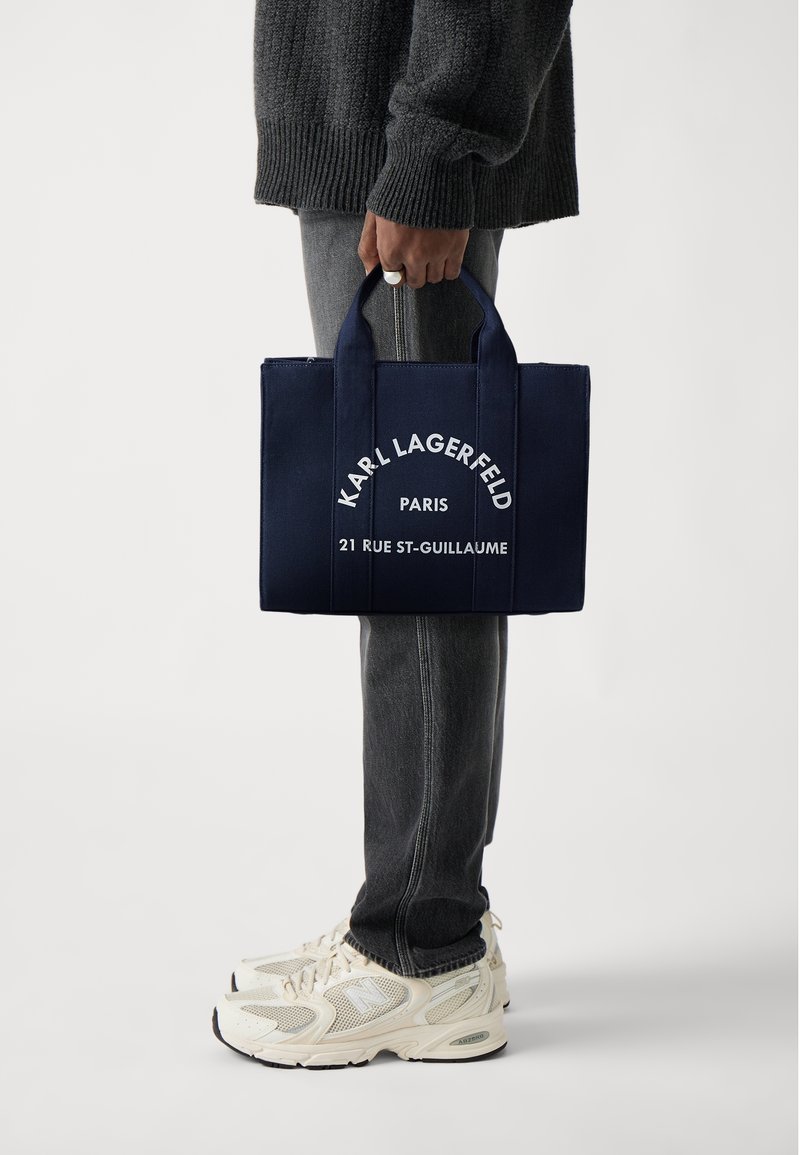 Canvas-totepåse i marinblått med vittryckt logotyp: "KARL LAGERFELD PARIS 21 RUE ST-GUILLAUME." Två robusta handtag, rektangulär form.