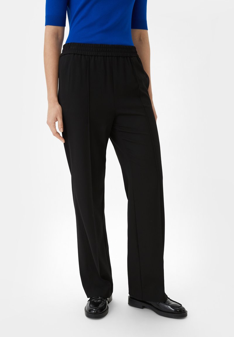 Zwarte wijde broek met elastische tailleband, voorzien van een gladde stoftextuur en zijnaaddetails. Draagt een blauwe top.