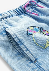 Pantalon en jean bleu clair avec taille élastique, cordon rose et bleu, poche latérale et détail cœur brodé coloré.
