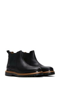 Botas Chelsea de cuero negro con acabado texturizado, paneles laterales elásticos y suela de goma resistente con ribete decorativo marrón.