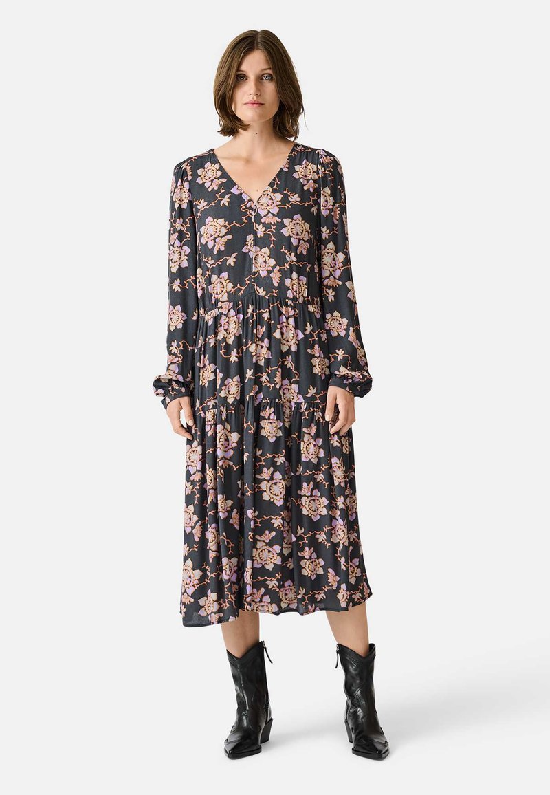 Floral-patterned, long-sleeve dress in dark fabric, featuring a V-neckline and tiered design, paired with black cowboy-style boots.