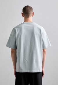 Světle modré bavlněné tričko s kulatým výstřihem a krátkými rukávy. Jednoduchý design bez viditelných vzorů nebo loga na zadní straně.