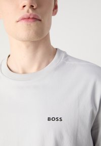 Szürke pamut póló kerek nyakkivágással és bordázott szélekkel, bal mellkason egy kis fekete "BOSS" logóval.