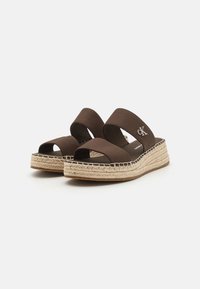 Brūni espadrilles sandales ar divām platām auduma siksnām, izstrādātas no austā jūts starpsoles un gumijas zoles. Sānos ir CK logs.