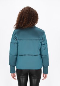Turkusowa kurtka puchowa o gładkiej teksturze, z wysokim kołnierzem, żebrowanymi mankietami i poziomymi przeszyciami dla lepszego ocieplenia. Przedstawiono widok z tyłu.