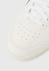 Valged nahast vabaajajalatsid, millel on perforatsioonid varbal, tekstureeritud pind, ümar varvas ja valged paelad. Silmapaistvad õmblused äärejoonel.