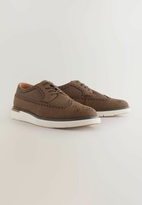 Zapatos de cuero marrón con diseños perforados, cierre de cordones y suelas de goma blanca. Los zapatos tienen una silueta estructurada y un acabado texturizado.