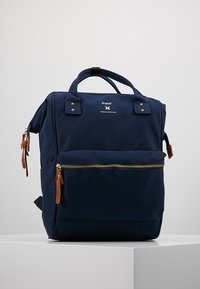 Navy modrý látkový batoh s dvěma horními uchy, přední kapsou na zip a hnědými koženými úchyty na zip. Disponuje elegantním designem a detaily loga.