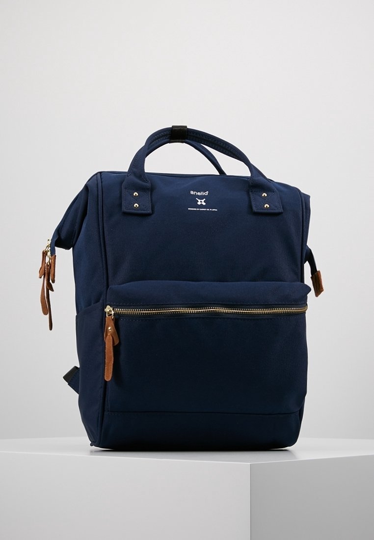 Navy modrý látkový batoh s dvěma horními uchy, přední kapsou na zip a hnědými koženými úchyty na zip. Disponuje elegantním designem a detaily loga.