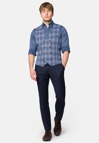 Szary i niebieski kamizelka w kratę na niebieskiej koszuli, w połączeniu z ciemnonawym spodniami i brązowymi butami. Kamizelka ma pięć guzików i spiczasty dół.