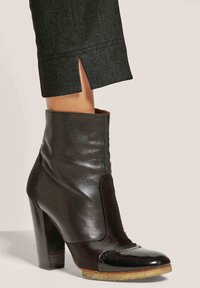 Schwarze Leder-Stiefelette mit hohen Absätzen, ausgestattet mit einer glatten Oberfläche und einem kontrastierenden Wildleder-Panel. Die Sohle ist hell gefärbt mit subtiler Textur.