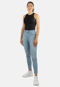 Schwarzes ärmelloses Oberteil im taillierten Stil, kombiniert mit hellblauen hochgeschnittenen Jeans. Weiße Sneaker vervollständigen den lässigen Look.