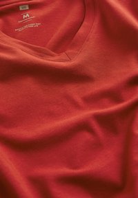 Röd bomullsblandning med V-hals, med en slät textur och synlig sömnad på kragen, märkt "M" för storlek.