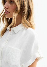 Camicia bianca con bottoni, dal finish testurizzato, caratterizzata da una sola tasca sul petto e maniche arrotolate. Design semplice e versatile.