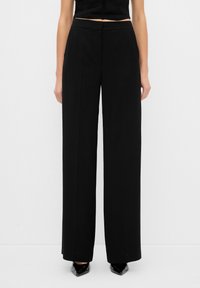Pantalons larges noirs en tissu lisse, avec une taille ajustée et des poches latérales discrètes. Le design présente des lignes épurées et une silhouette élégante.