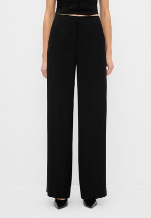 Pantalons larges noirs en tissu lisse, avec une taille ajustée et des poches latérales discrètes. Le design présente des lignes épurées et une silhouette élégante.