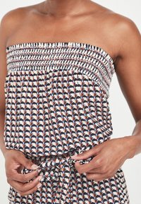 Stropfri, mønstret top med smocket liv i marineblå, hvid og orange nuancer; bundet talje detaljer giver form. Blødt, letvægtsstof.