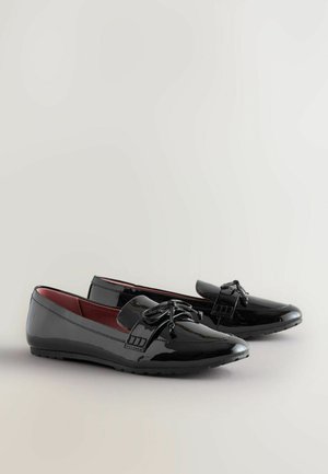 Schwarze Lackleder-Slipper mit glatter Oberfläche, Schleifenakzent und rotem Innenfutter. Flache Sohle und runde Zehenform für legere Looks.
