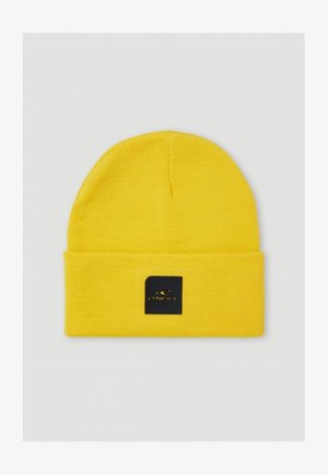 Bonnet tricoté jaune avec un revers replié, comportant une étiquette carrée noire avec le logo de la marque en or. Texture lisse et design ajusté.