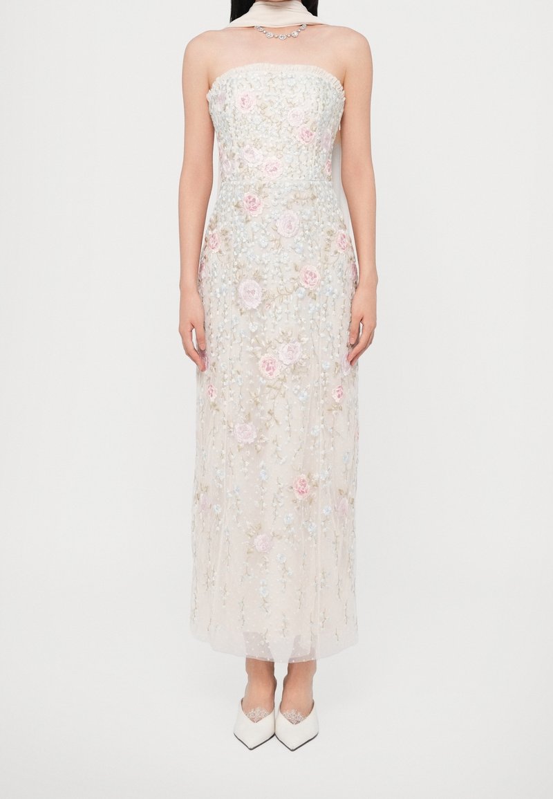Robe transparente sans bretelles avec broderie florale, fleurs rose pâle et bleues, longueur cheville, associée à des chaussures blanches pointues et un collier.