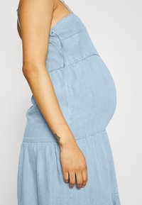 Veste maxi sem mangas em azul claro, feita em tecido suave com uma cintura império e saia franzida. Apresenta um fecho lateral e bolsos angulados.