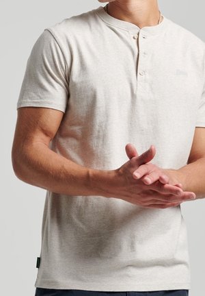 Koszulka henley z krótkim rękawem w jasnobeżowym kolorze, z dwuklapkowym zapięciem na guziki, subtelną fakturą oraz małym logo na piersi. Prosty krój.