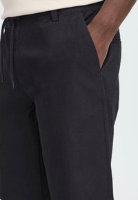 Shorts en coton noirs avec une taille élastique et un cordon de serrage, dotés de poches latérales et d'une texture lisse.