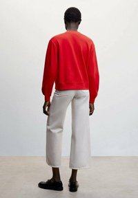 Sweat-shirt en coton rouge avec des poignets et un ourlet côtelés, associé à un pantalon en denim blanc à jambes larges. Des mocassins noirs complètent la tenue.