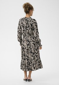 Rochie lungă cu imprimeu negru și bej, cu mâneci lungi, strânsă în talie, având un tiv evazat și un material texturat.