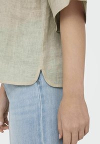 Lys beige linned skjorte med korte ærmer, har en afrundet kant og er parret med lyseblå denim. Søm detaljeret i siden.