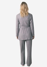 Ensemble de détente en gris côtelé comprenant un haut à manches longues et un pantalon large, avec une taille ceinturée et un tissu texturé.