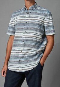 Koszula z krótkim rękawem z jasnoniebieskimi, białymi i ciemnoszarymi paskami, wykonana z teksturowanej tkaniny. Posiada kołnierzyk zapinany na guziki oraz guziki z przodu.