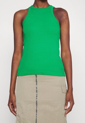 Person iført en ærmeløs grøn ribstrikket tanktop kombineret med et beige skørt med lynlås foran og sidelommeklap.