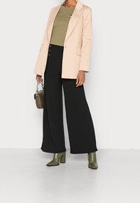 Blazer in licht perzik, olijfgroene t-shirt, wijde zwarte pantalon en donkergroene laarzen met krokodillenpatroon. Gestructureerd, modern ontwerp.