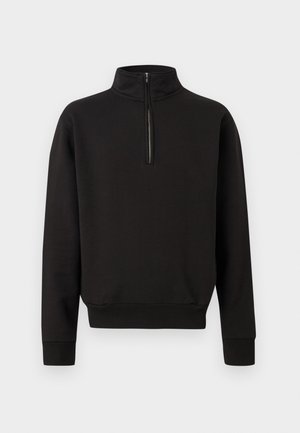 Schwarzer Langarm-Pullover mit halbem Reißverschluss vorne, hohem Kragen, gerippten Bündchen und Bund vor einem schlichten, hellen Hintergrund.