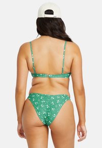 Grön blommig bikini med tunna justerbara remmar, prydd med ett mönster av små vita blommor och en strukturerad tygfinish.