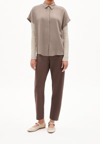 Beige kortärmad blus med krage, lager på lager över en ribbad beige tröja. Bruna smala byxor och ljusa ballerinas med rem.