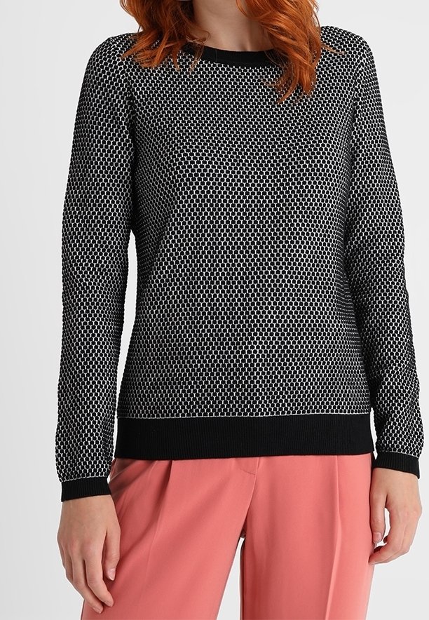 Femme portant un pull à manches longues à motifs noir et blanc avec des poignets noirs et un pantalon large couleur corail rose.