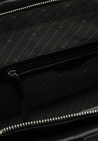 Interno di una borsa nera in pelle con una tasca con cerniera, caratterizzato da una fodera testurizzata e sottili strisce diagonali, hardware della cerniera in argento.