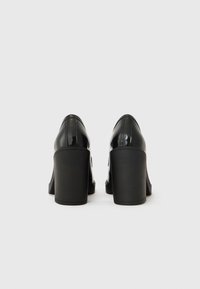 Chaussures à talons hauts en cuir verni noir avec un bout rond, un talon bloc épais et des coutures visibles le long des coutures.