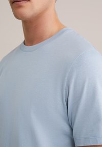 Világoskék rövid ujjú pamut póló kerek nyakkivágással. Puha textúrájú, minimális varrással, laza szabással.