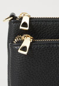 Borsa in pelle nera texture con due zip dorate che presentano un design a taglio triangolare, cucita in modo sicuro e dall'aspetto elegante.